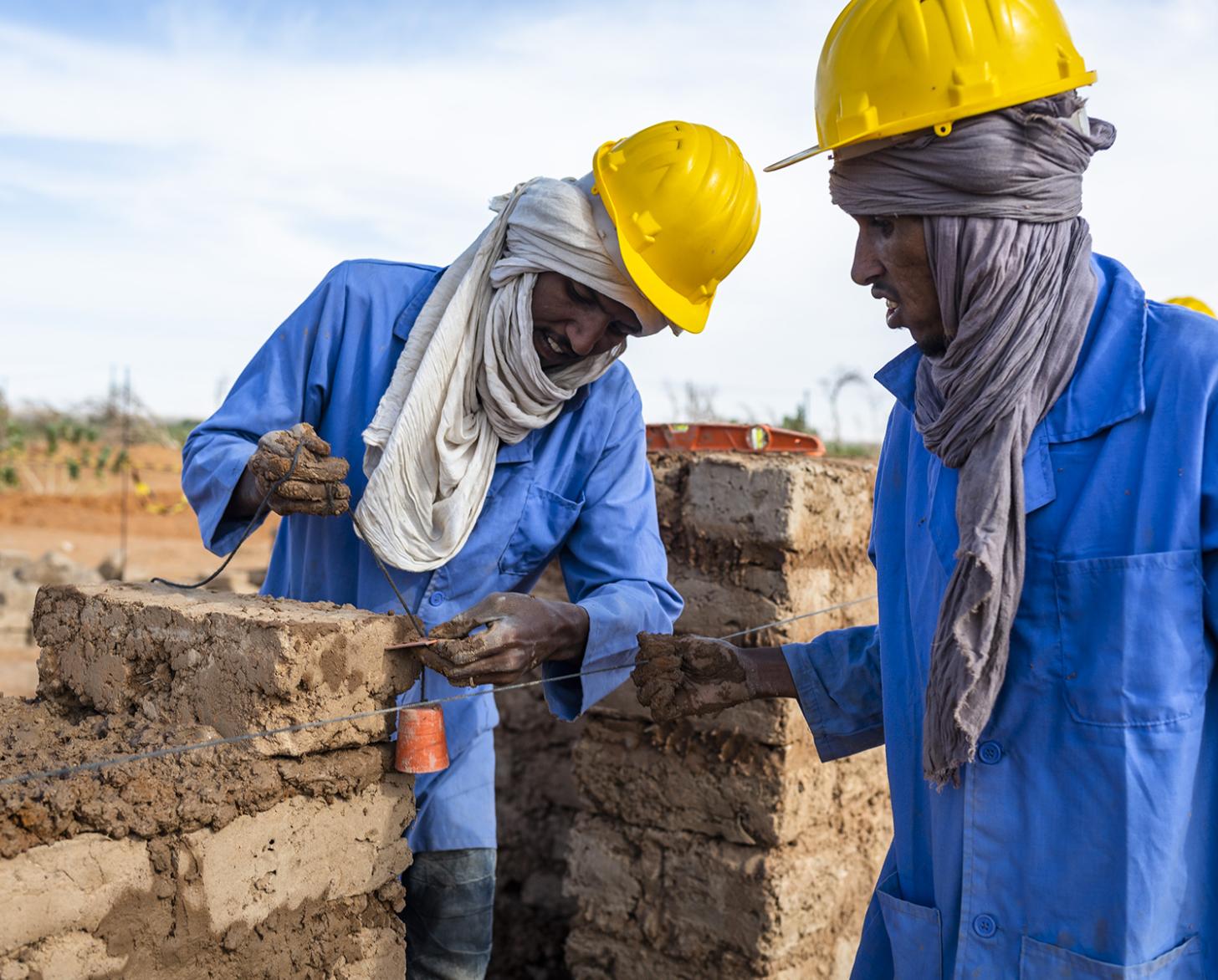 Dos personas con casco examinan ladrillos en una obra de construcción.