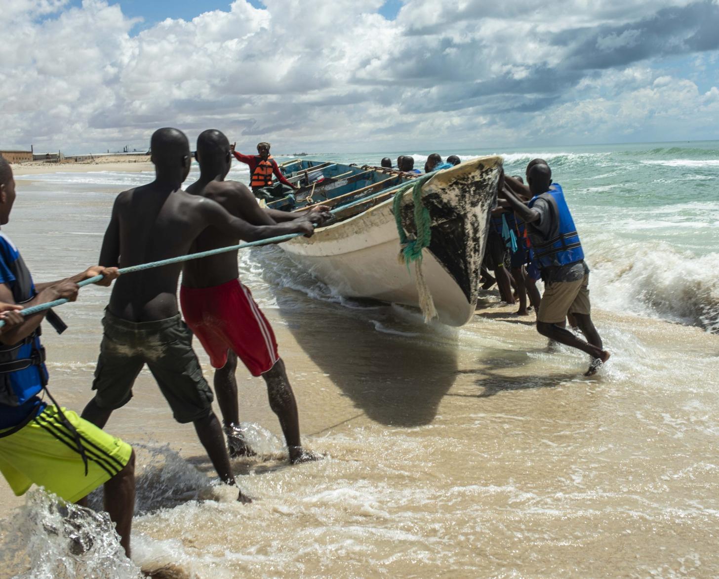 Varias personas trabajan juntas para sacar un barco del océano.