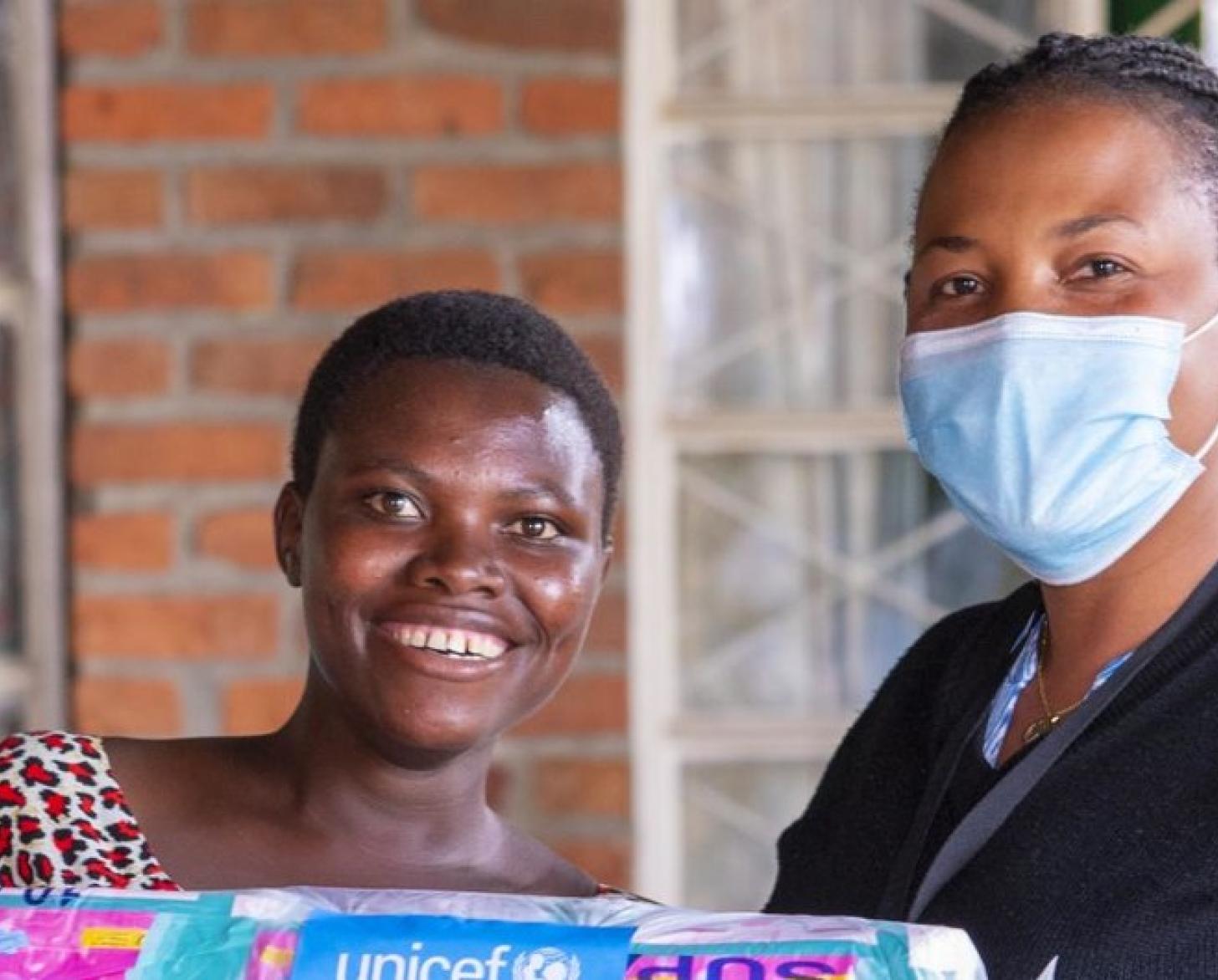 Deux femmes africaines, dont une portant un masque de protection respiratoire, se tiennent côte à côte devant l’objectif en souriant. 