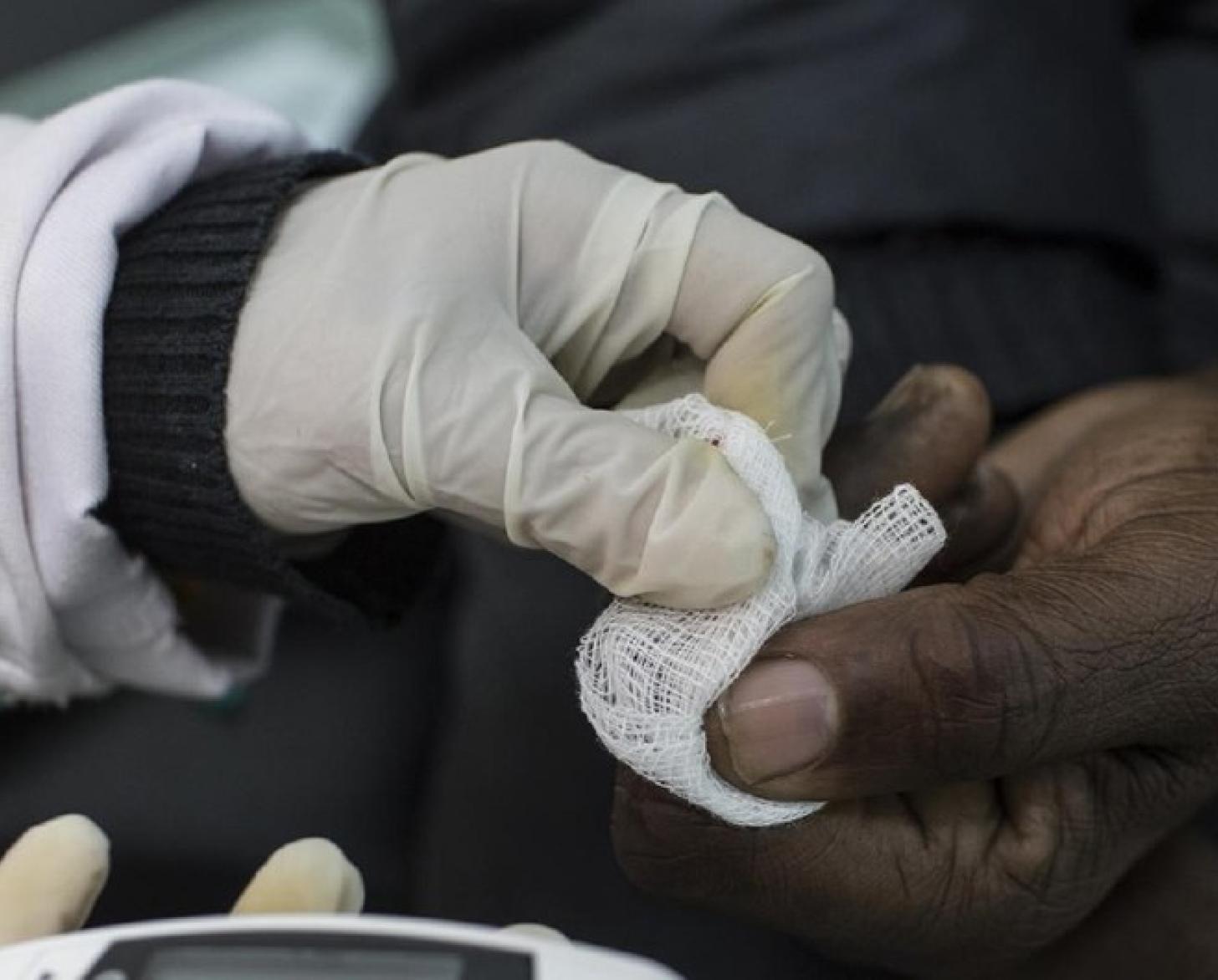 Gros plan sur la main gantée d'un professionnel de santé effectuant un test de dépistage du diabète en Afrique.