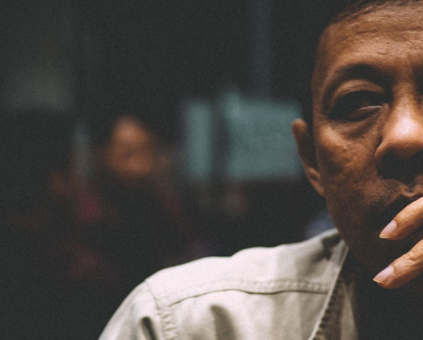Gros plan sur le visage d'un homme d'origine asiatique en train de fumer une cigarette dans une pièce sombre.