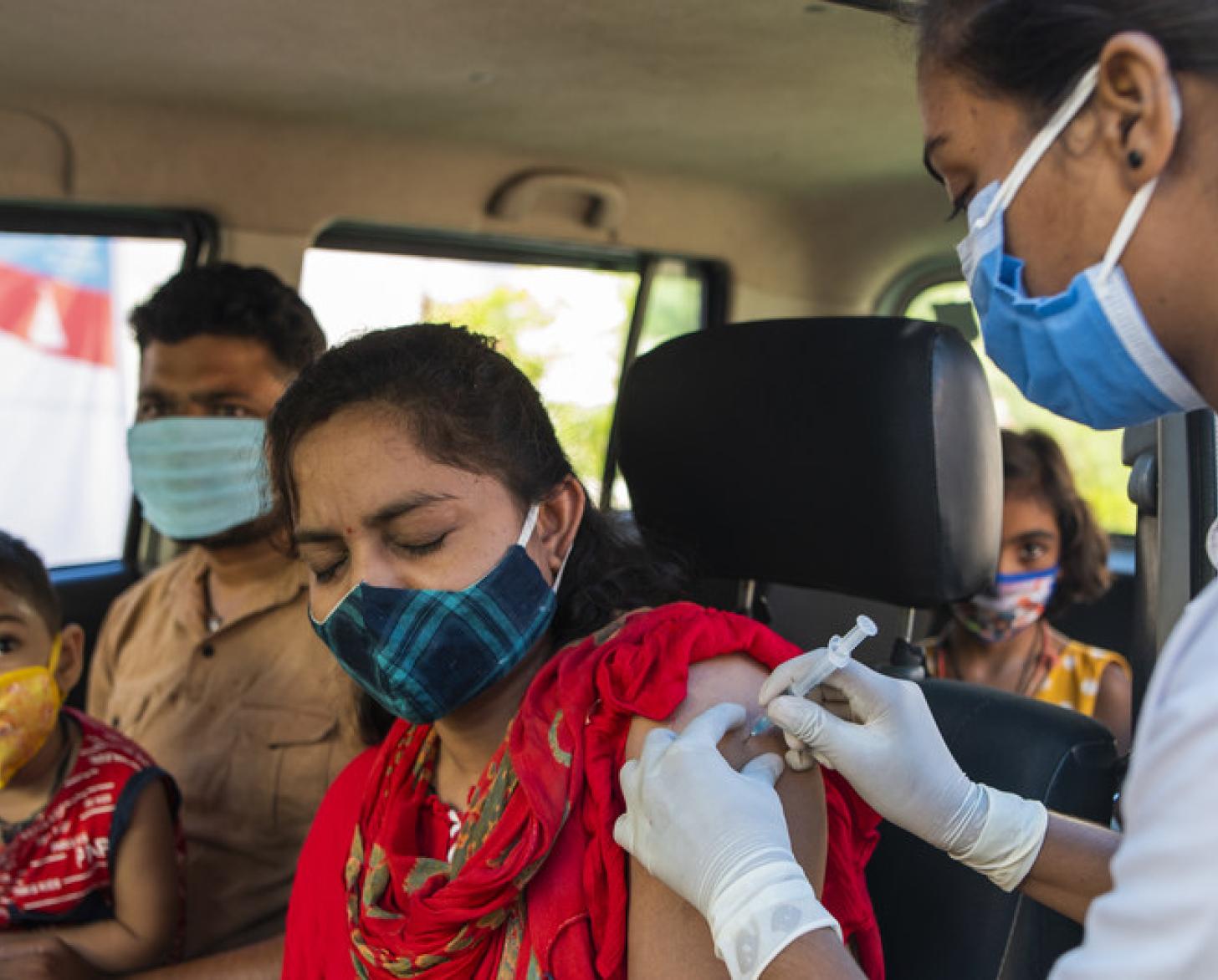 امرأة تتلقى اللقاح صد كوفيد-19 في السيارة وبجانبها رجل وطفل في حضنه.