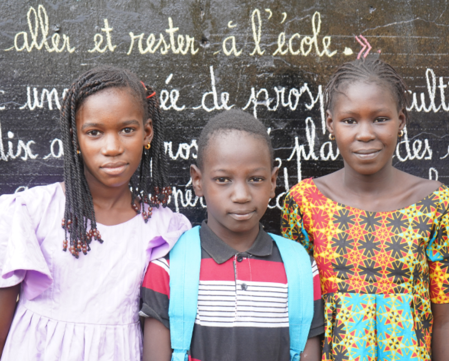 三个孩子站在一块黑板前直视镜头。