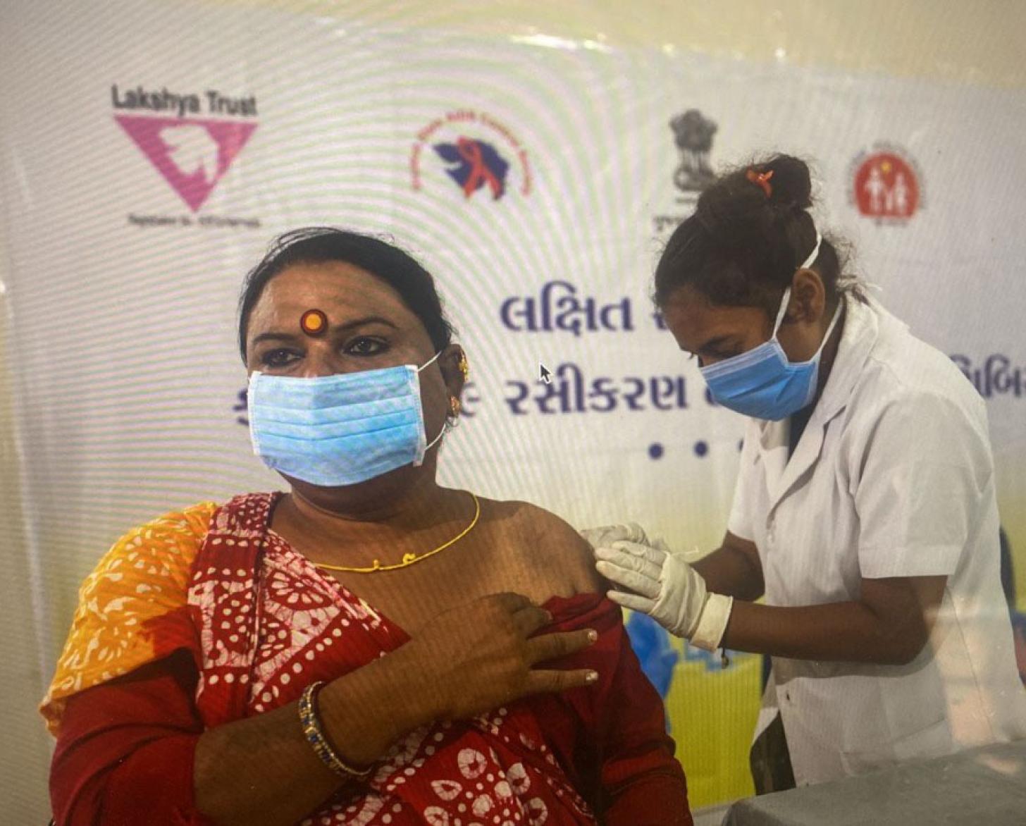 امرأة ترتدي كمامة زرقاء تتلقى لقاحًا من إحدى العاملات في مجال الرعاية الصحية.