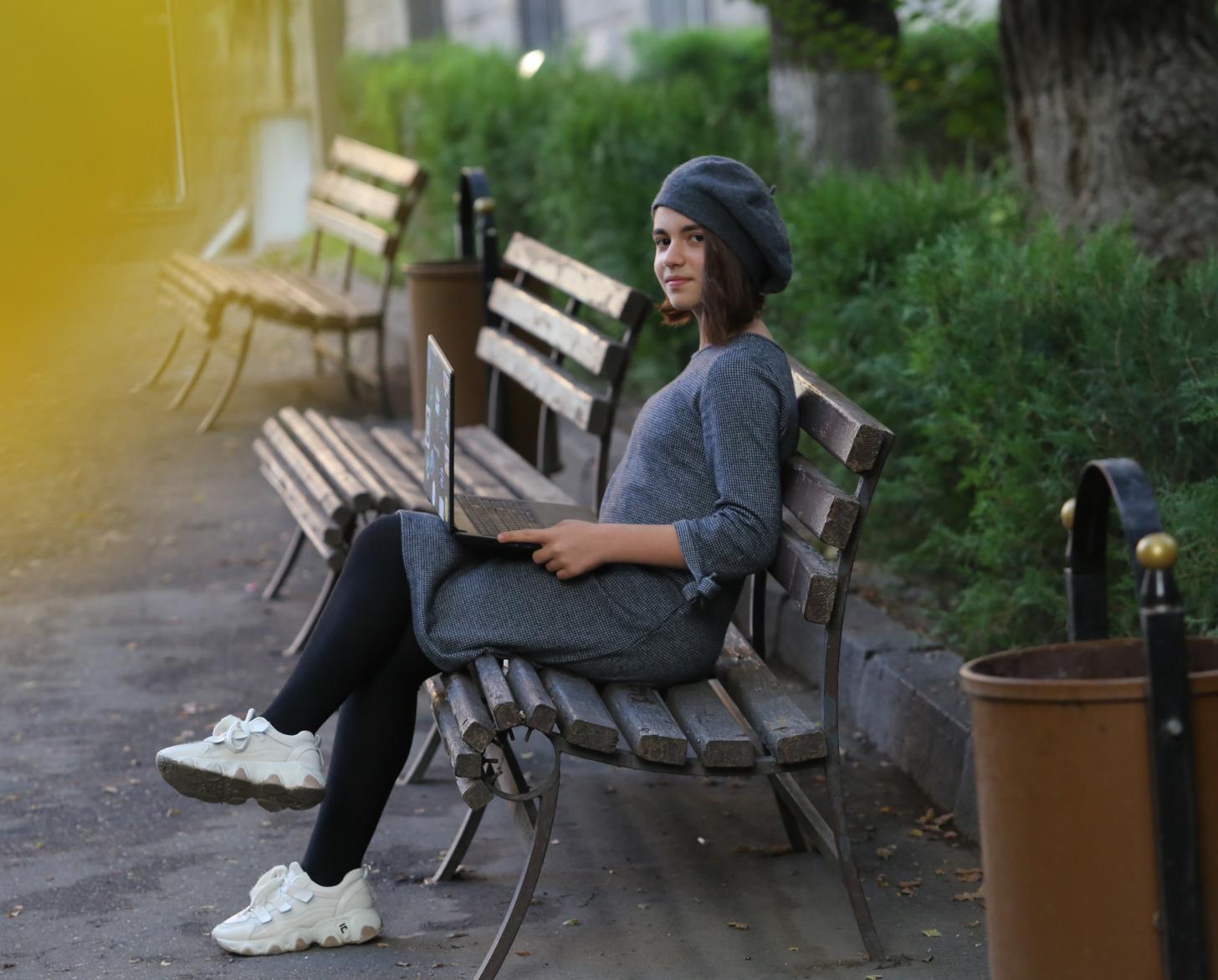 一位年轻女子坐在公园的长椅上，拿着一台笔记本电脑