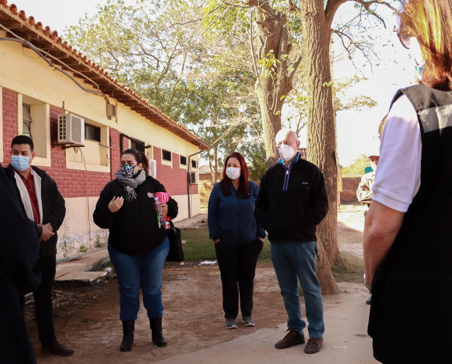 Un grupo de personas con mascarillas conversan en la parte externa de una edificación.