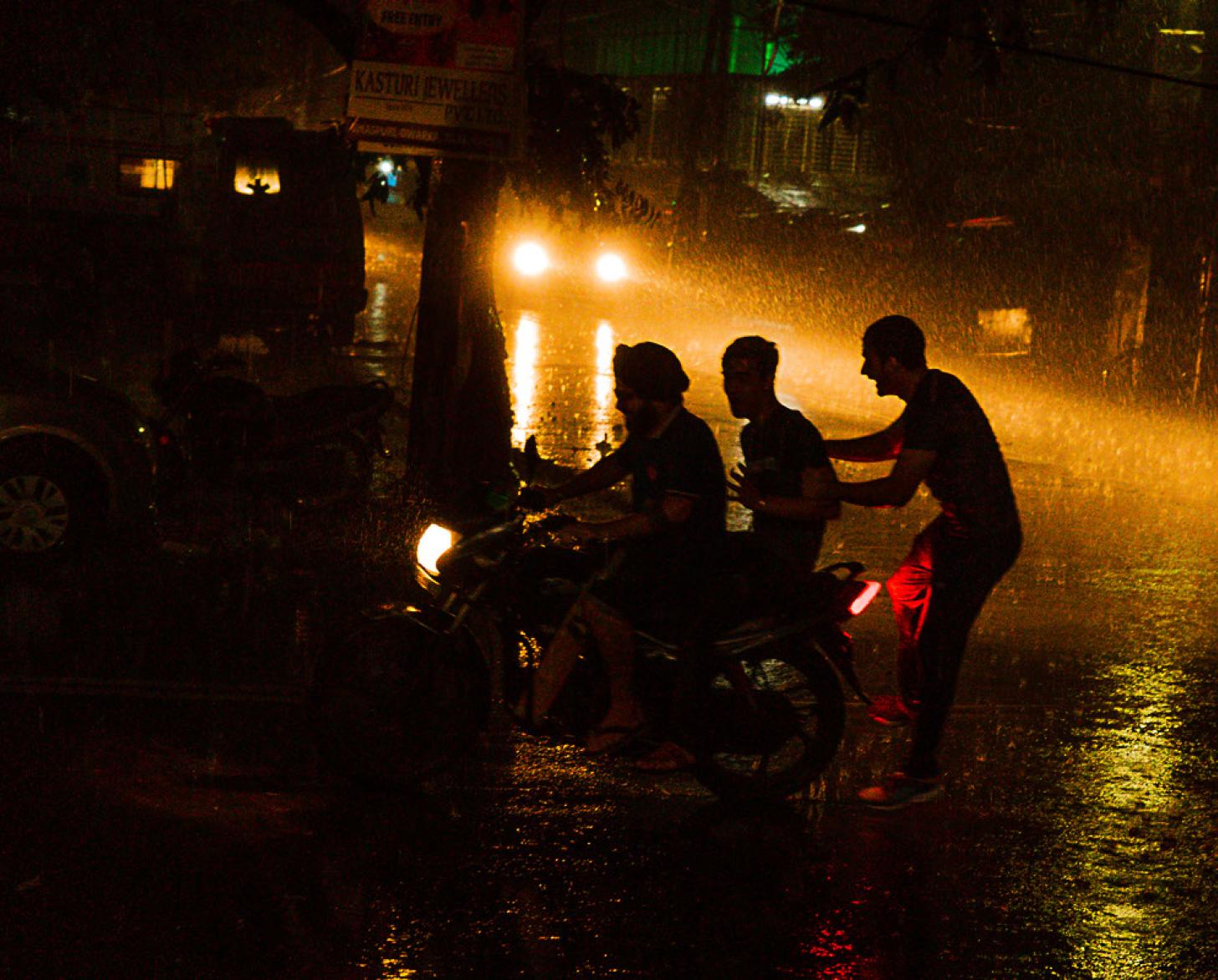 ثلاثة أشخاص يضحكون تحت المطر في الشارع ليلاً.