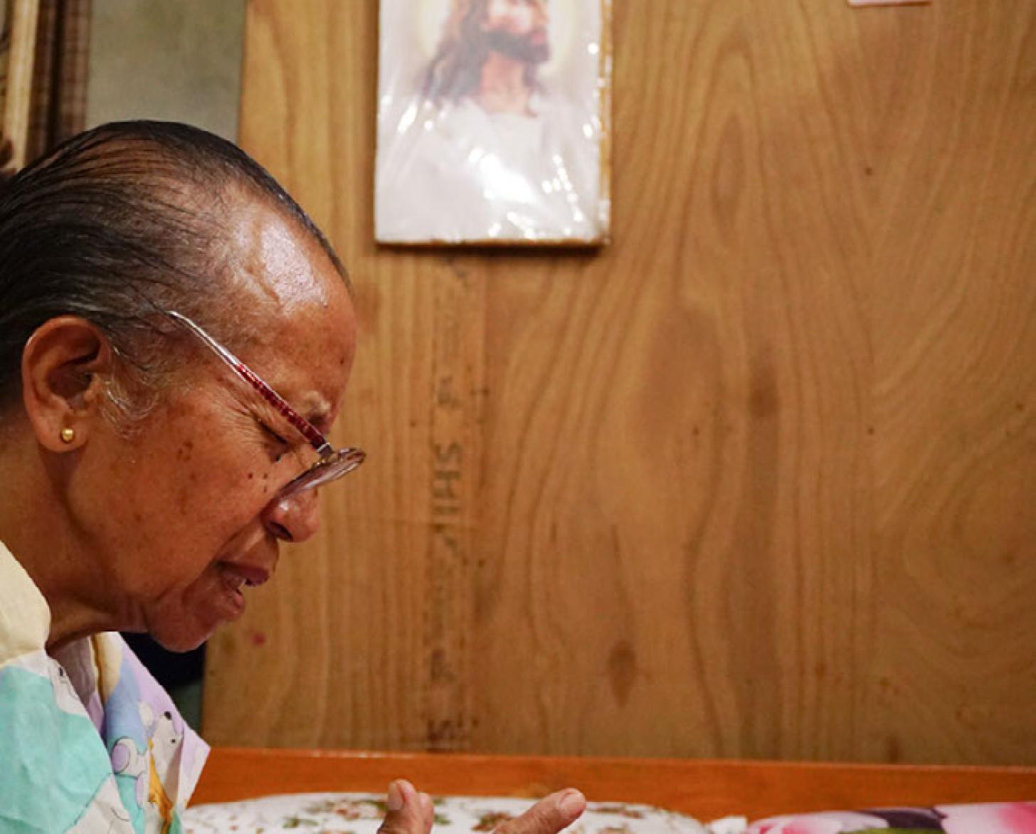 امرأة عجوز تجلس وتصلي أمام الكتاب المقدس المفتوح على الطاولة.