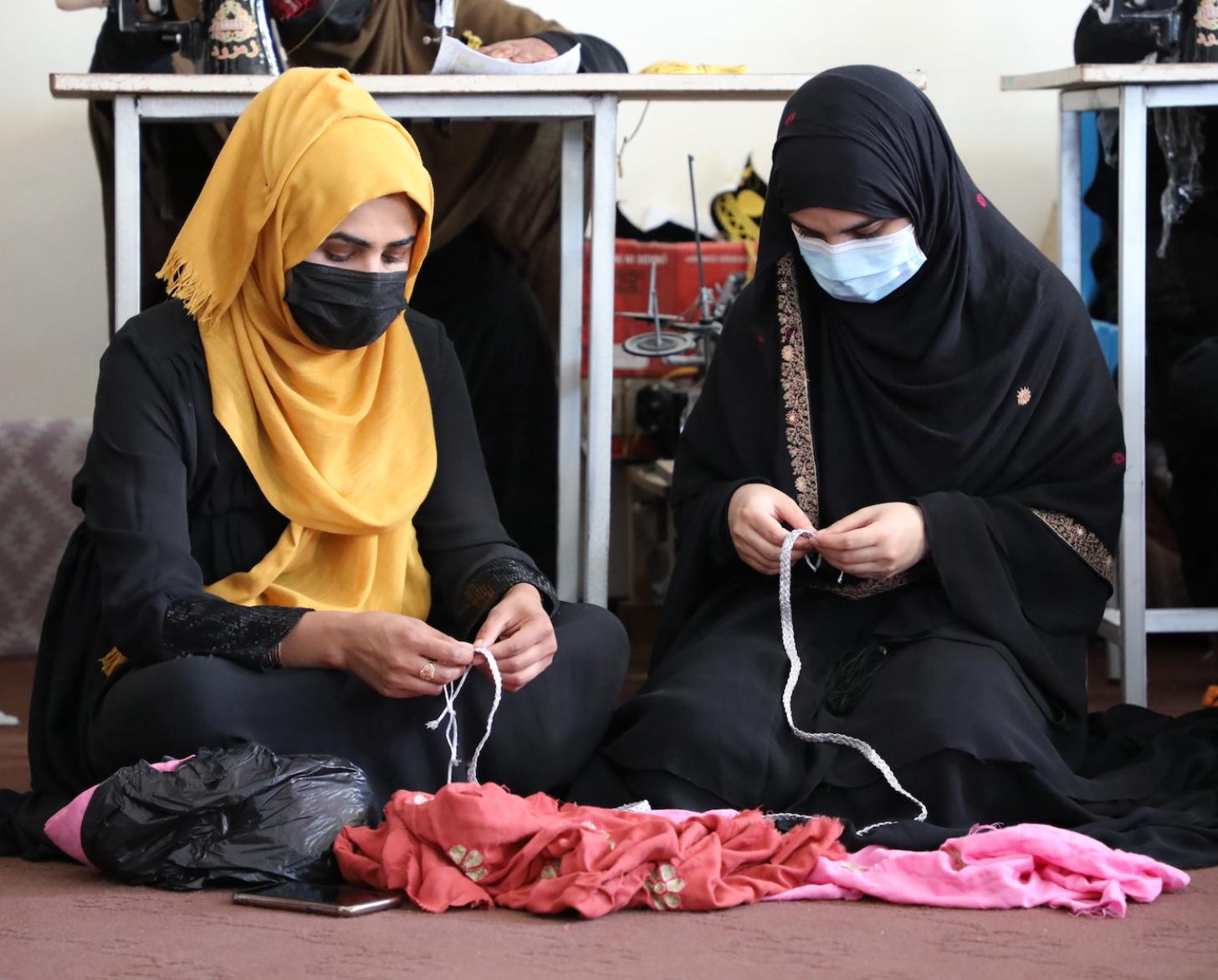 Dos mujeres con hiyab sentadas en el suelo aprendiendo técnicas de confección.