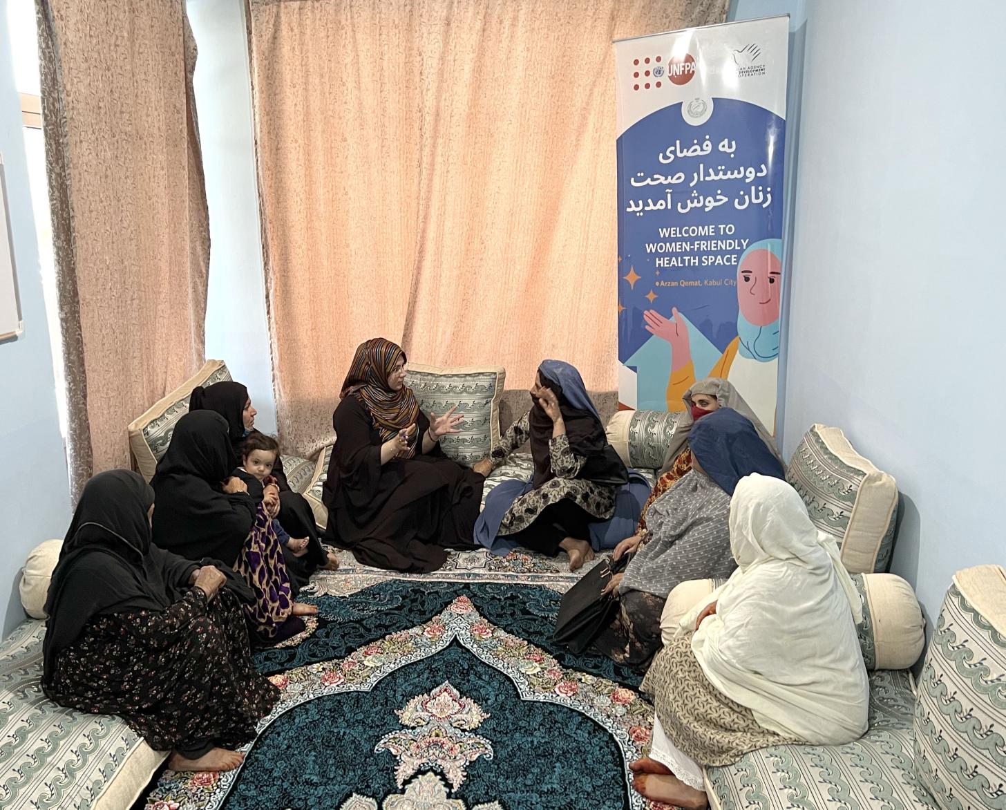 Ocho mujeres con hijab sentadas en medio círculo, una habla mientras las otras escuchan.