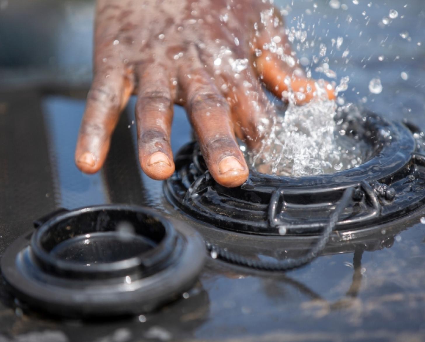 لقطة مقرّبة ليد رجل تتناثر حولها المياه المتدفقة من خزان.