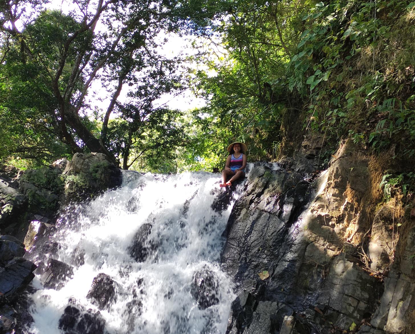 Una mujer sentada en medio del borde de una pequeña cascada en un área verde.