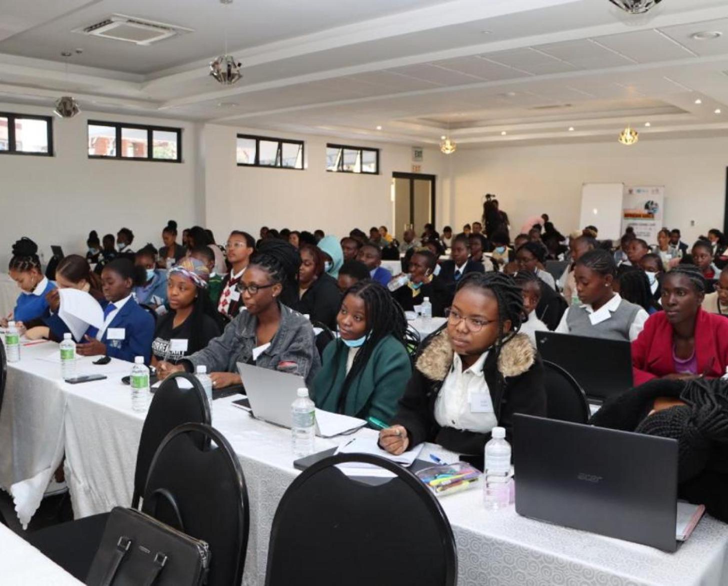 تجلس الفتيات في غرفة، أمام أجهزة الكمبيوتر، يستمعن بعناية إلى المدرب خلال دورة التشفير.