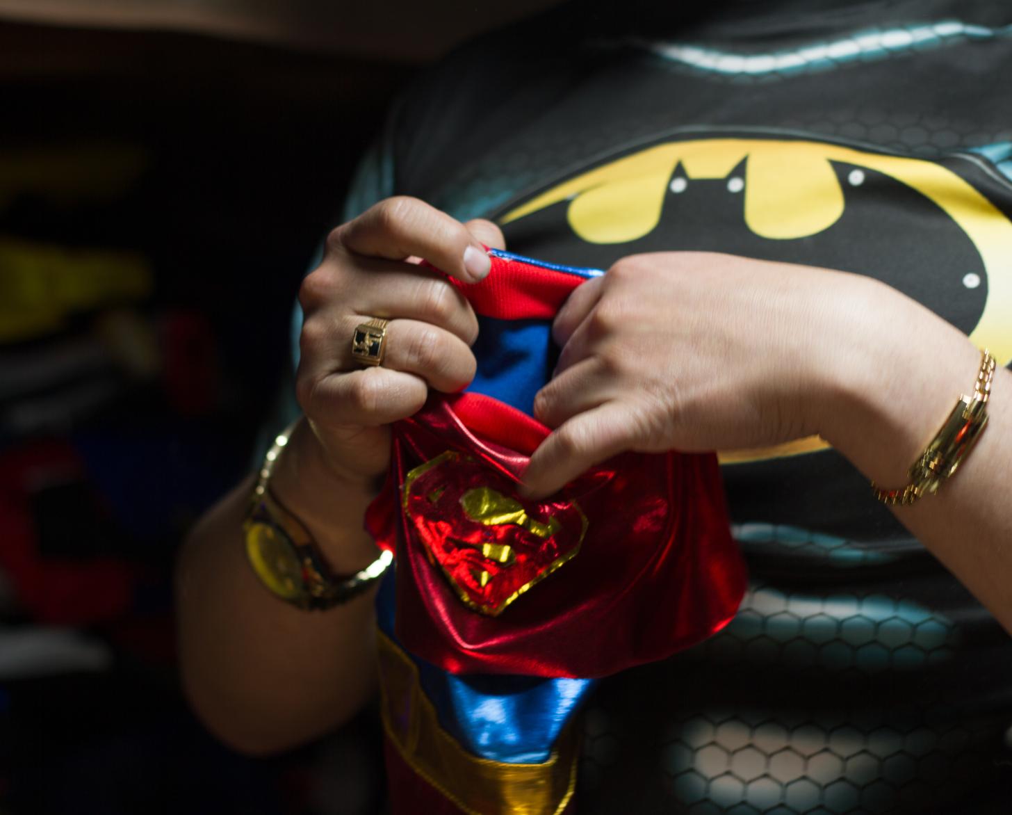 Plano detalle de dos manos que sostienen un disfraz de superhéroe para un pequeño perro.