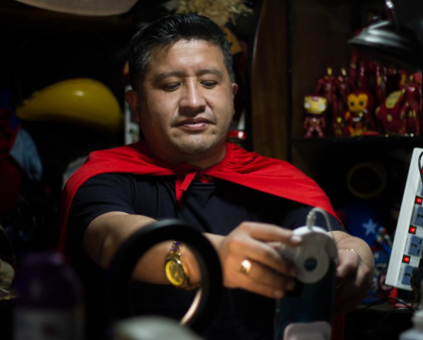 Un hombre con una capa roja de superhéroe, ajusta la lente de una cámara web.