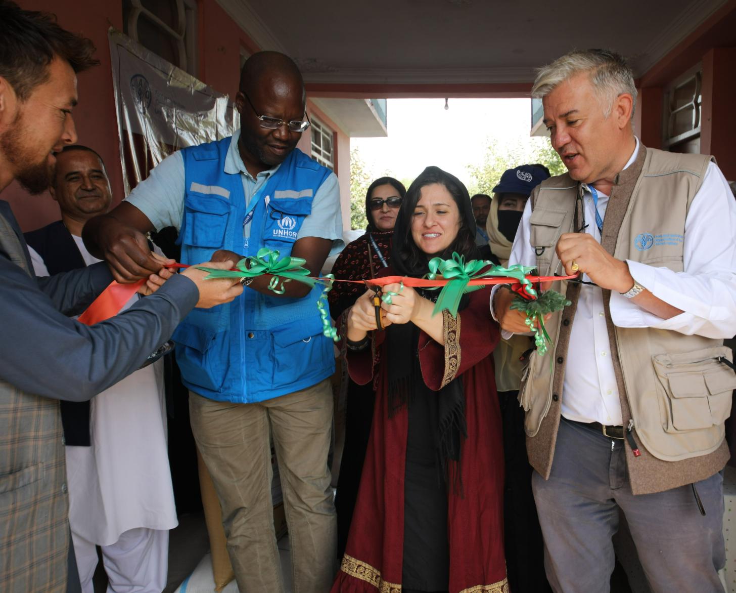 امرأة تستخدم مقصًا لقص شريط يمسكه رجلين على جانبيها.