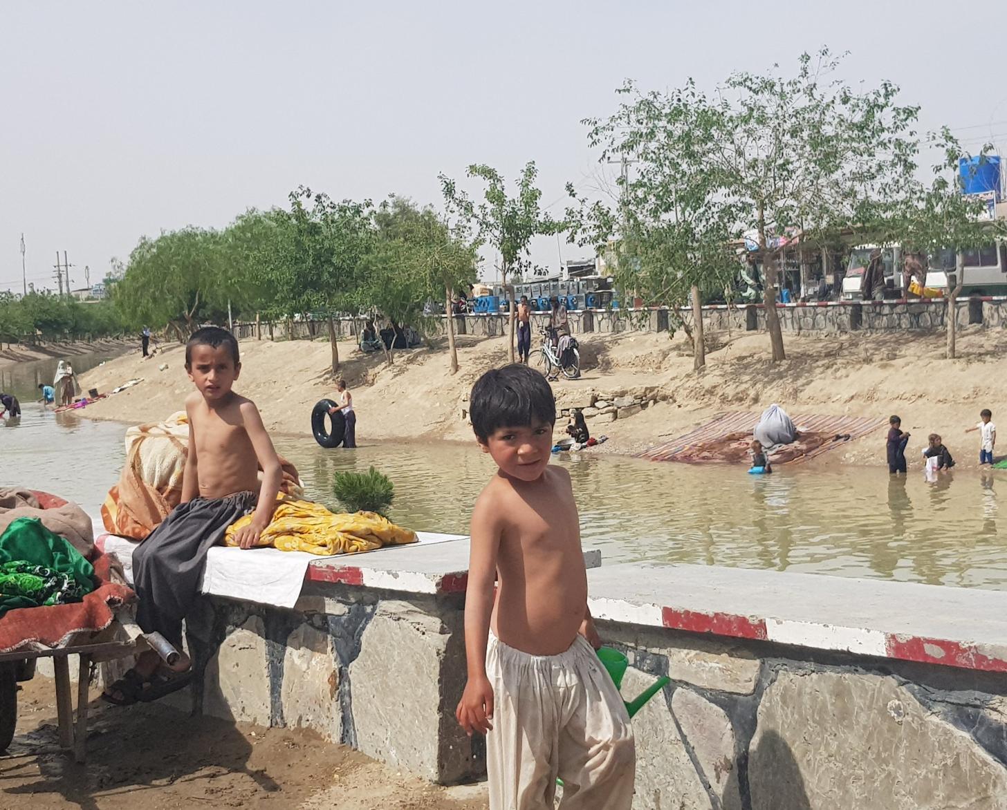 يلعب الأولاد الصغار في بحيرة مائية صغيرة محاطة بالعشب والأشجار.