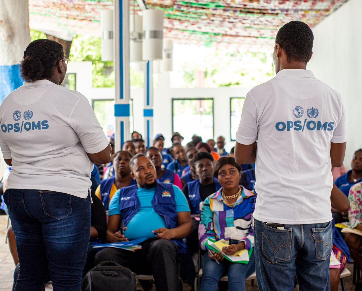 اثنان من موظفي منظمة الصحة للبلدان الأمريكية / منظمة الصحة العالمية، يتحدثان إلى العاملين الصحيين المجتمعيين في غرفة التدريب.