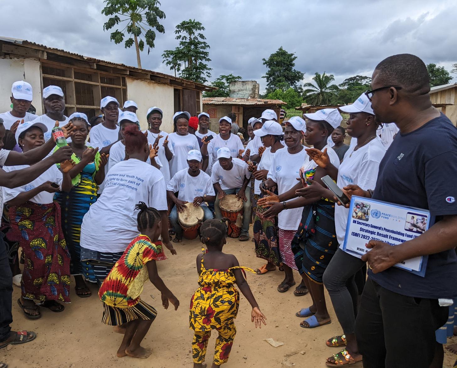 ترقص امرأة وفتاتان في وسط حلقة من الناس يرتدون قمصانًا وقبعات بيضاء.