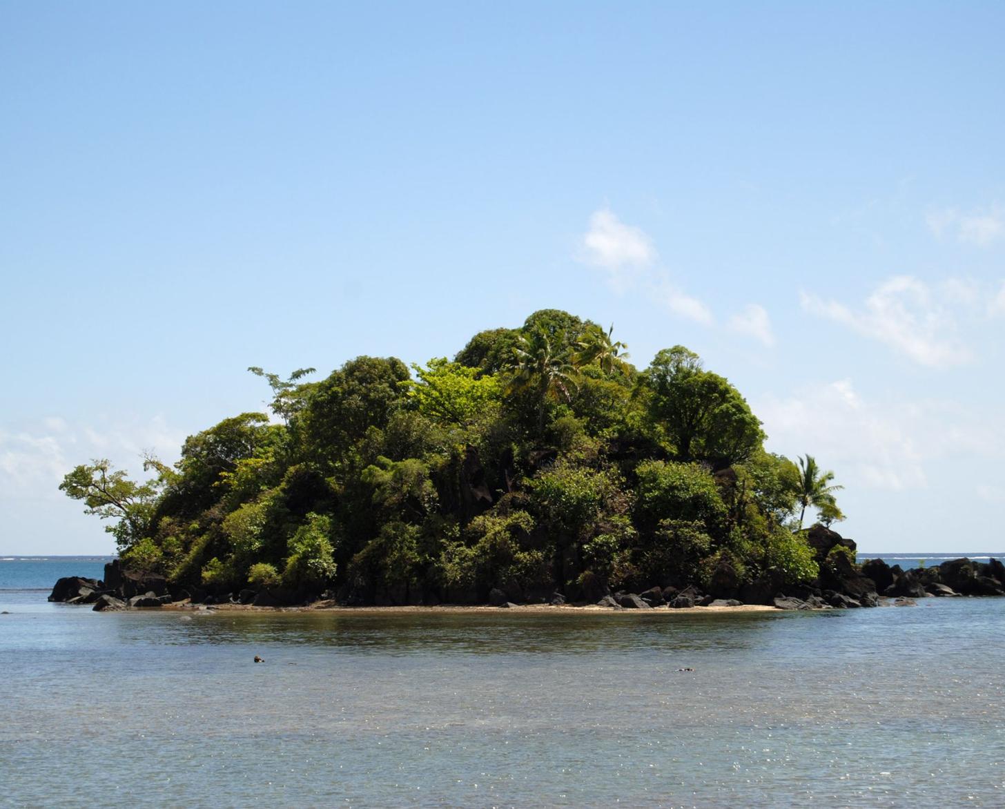 A close-up of a tiny island and light blue water around it.