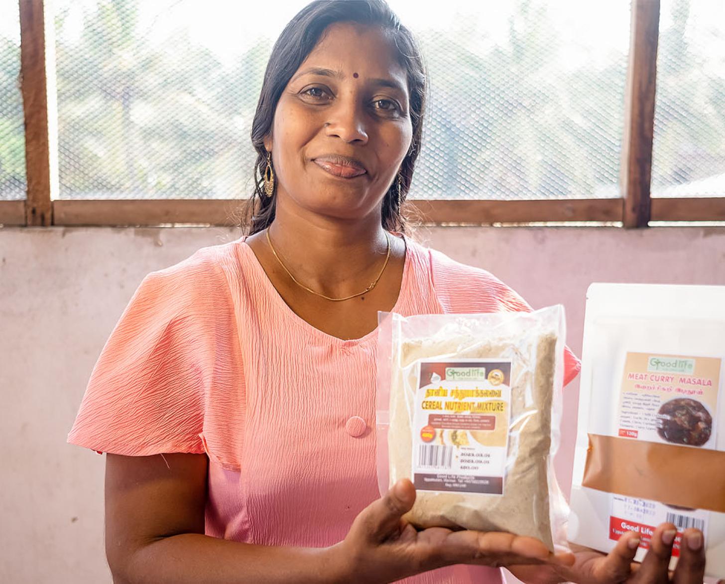A woman in a light pink top holds some of the products she makes, at her store in Sri Lanka.