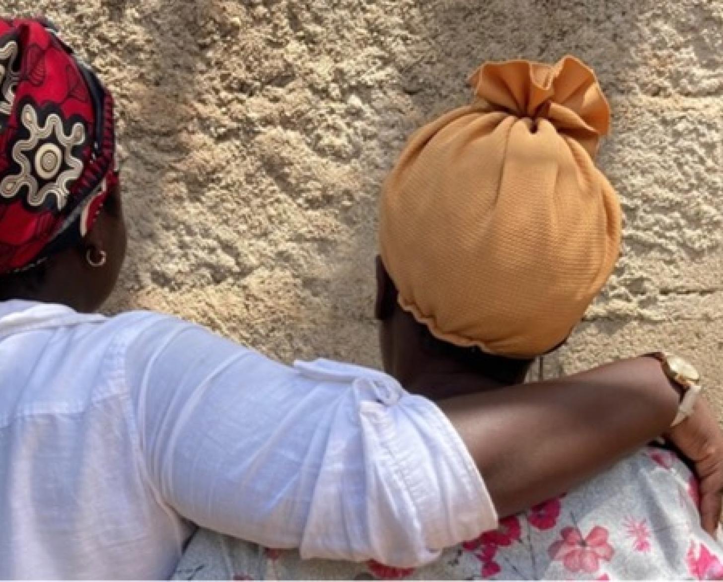two women in headscarves stand with their backs to the camera, one with her arm over the other 