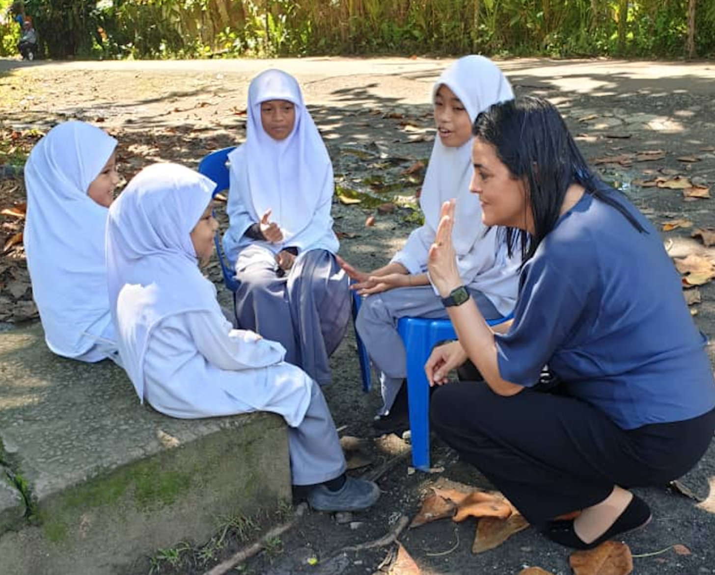 young children in white headscarves speaks with a woman leaning down on one knee