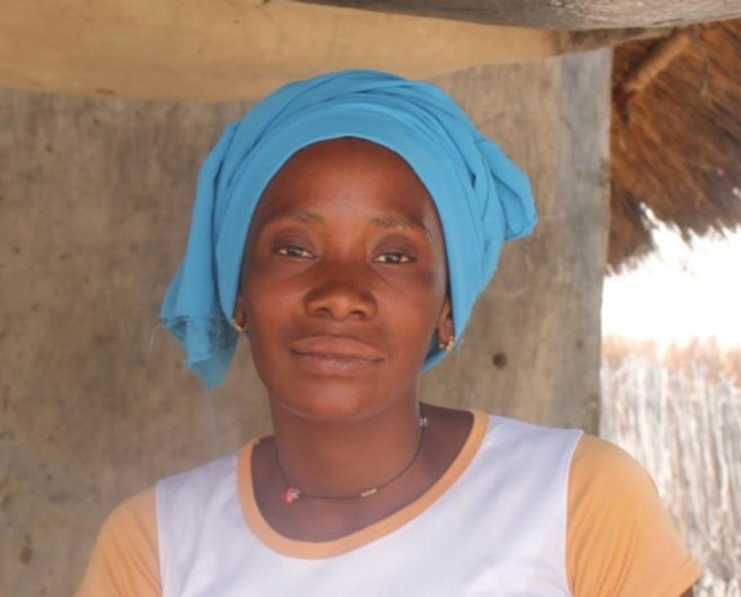 Портрет женщины в голубом головном платке на фоне дома с соломенной крышей