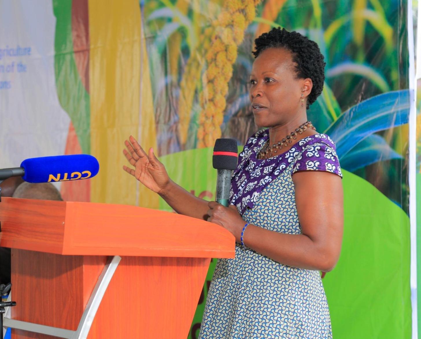 woman speaks at orange podium against a colourful wall 