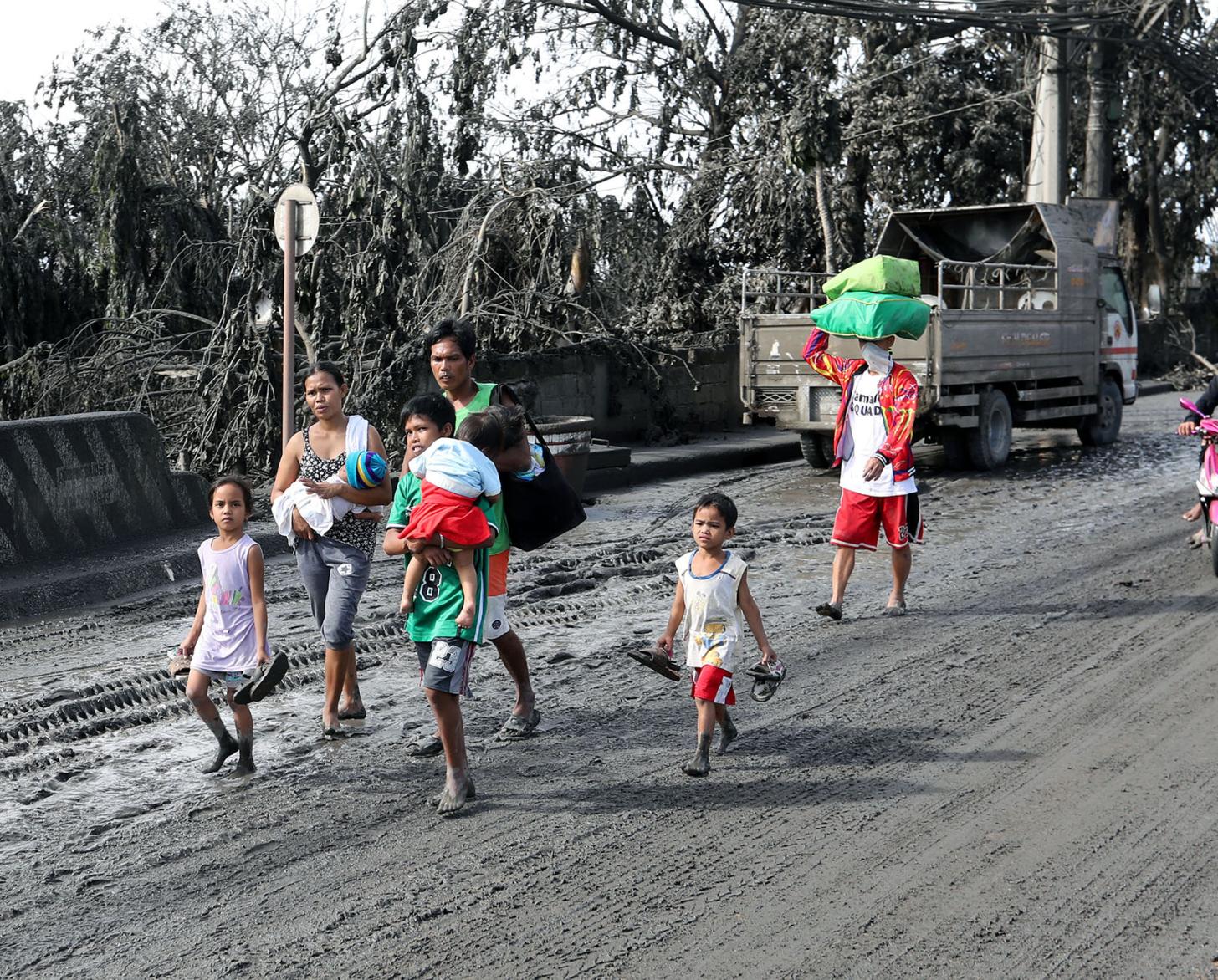 A family affected by the eruption of the Taal volcano in 2020 walks in volcanic ash-covered streets.
