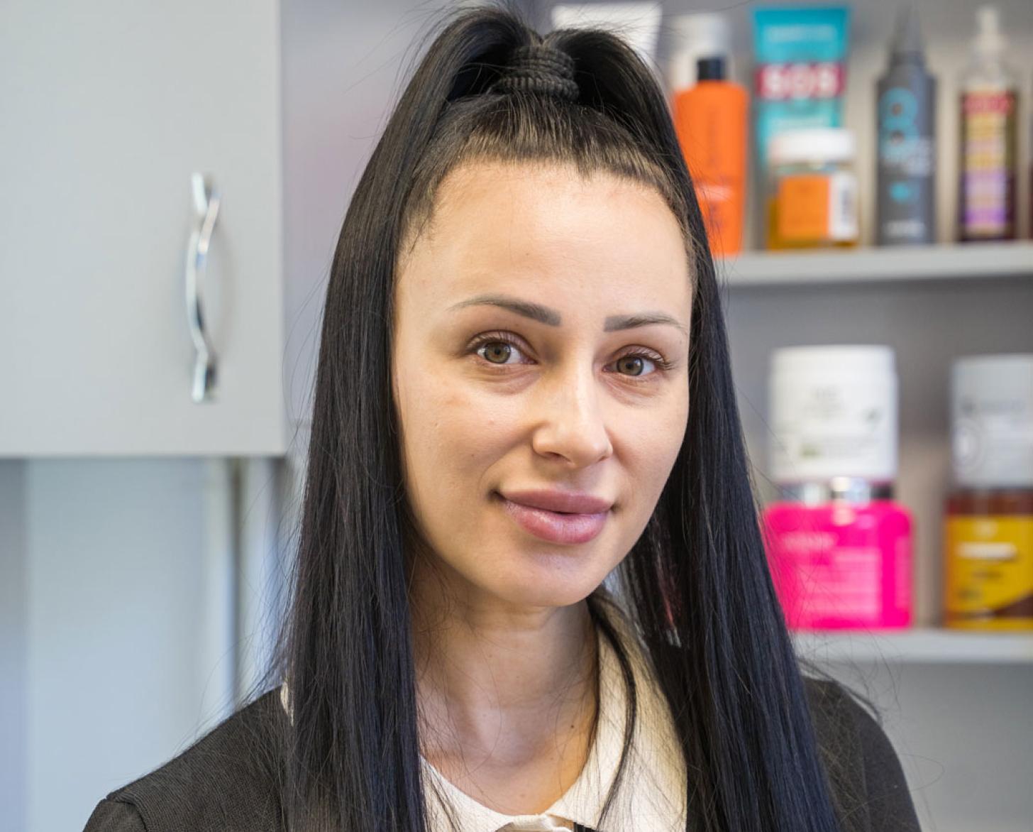 A woman stands in front of a shelf with beauty salon supplies.