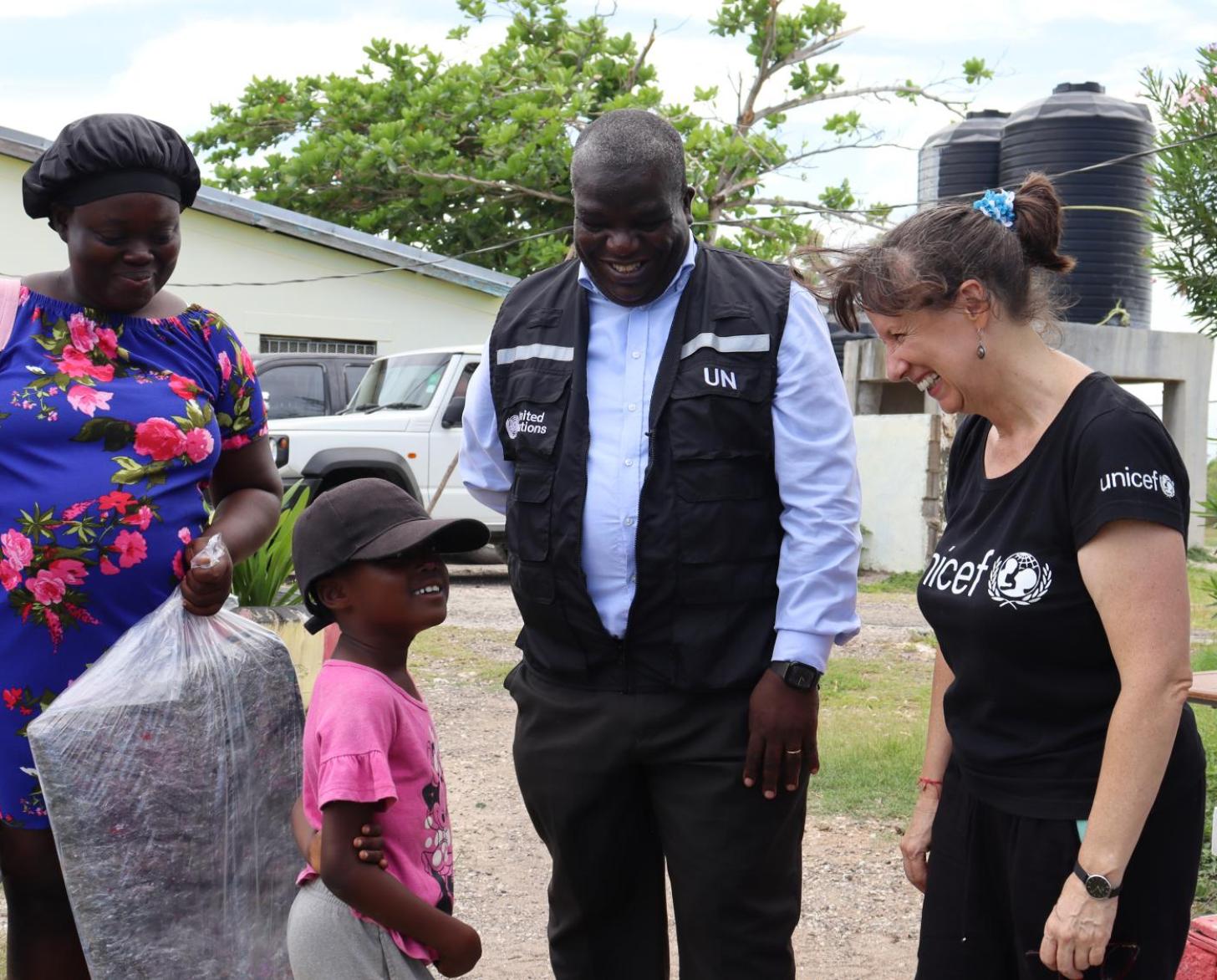 A man and a woman watch a little child carrying a bag