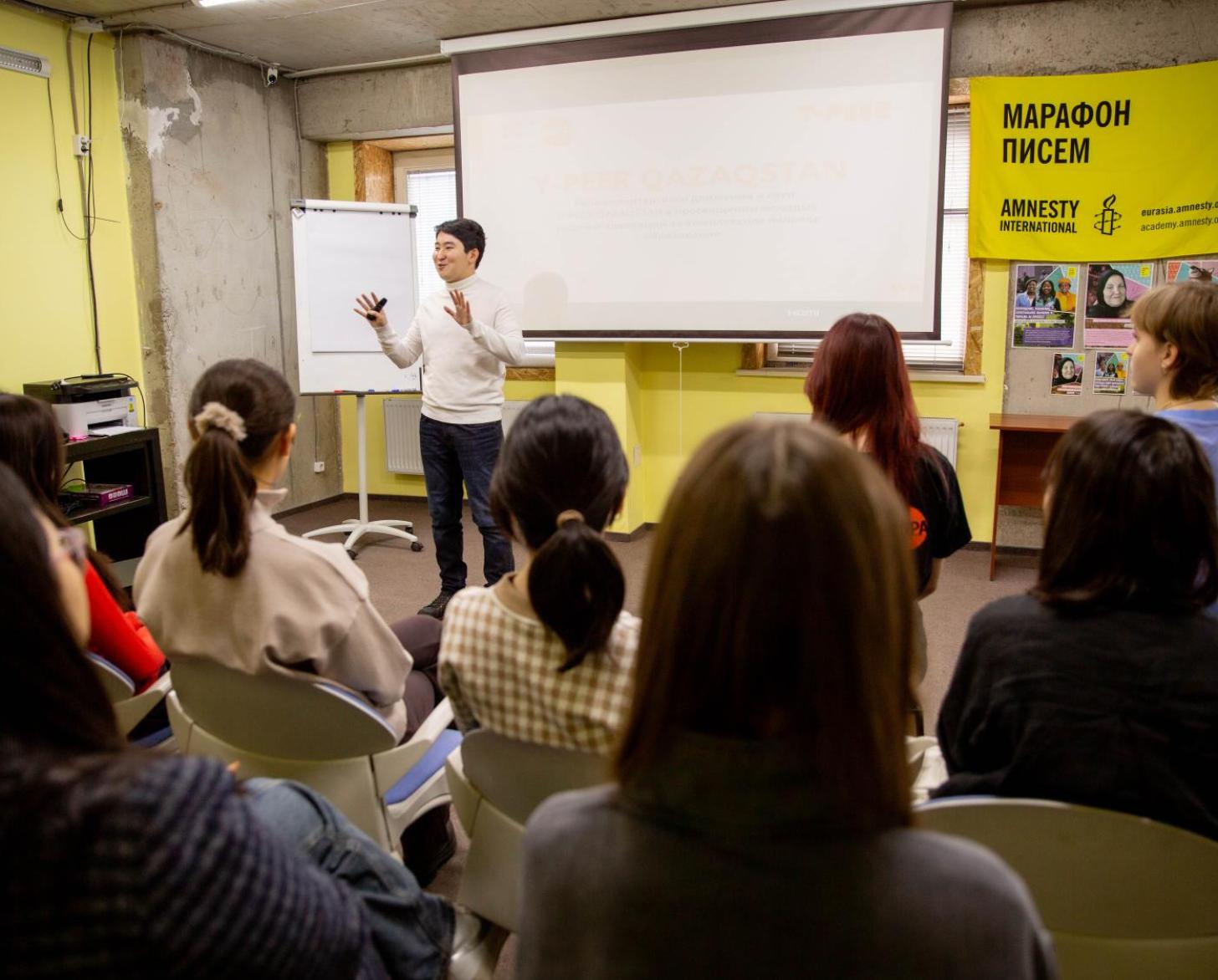 A man is in front of a large classroom speaking to students