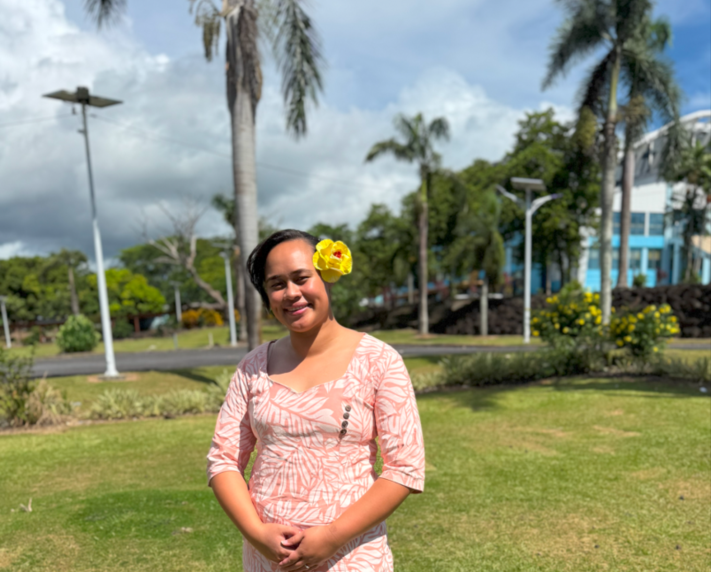A person wears a colorful dress in front of a green field with trees.