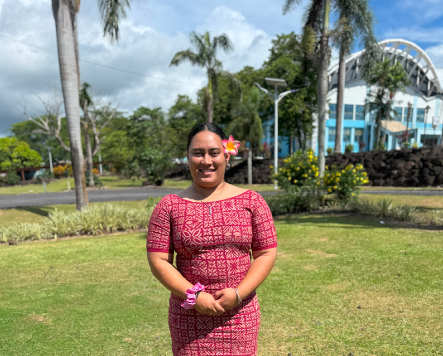 A person wears a colorful dress in front of a green field with trees.