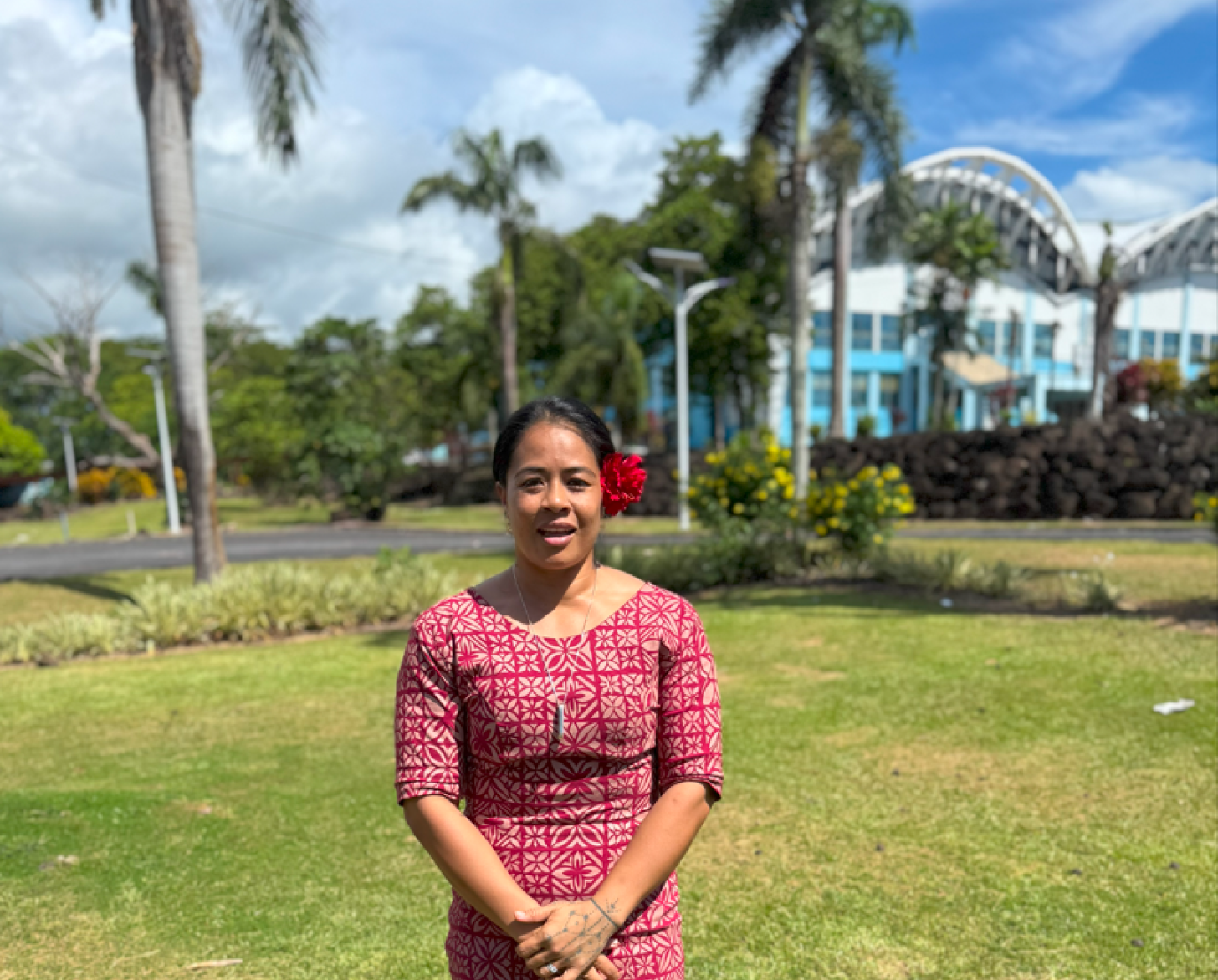 A person in a colorful dress stands in front of a green field with trees