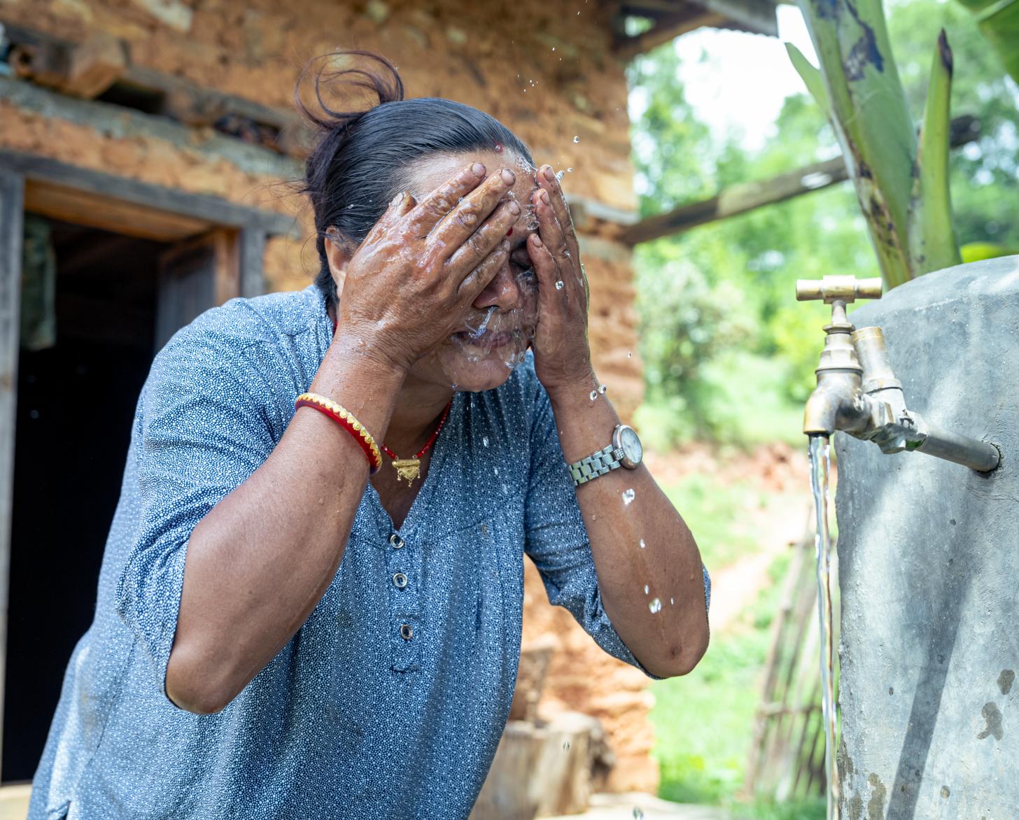 A woman washes her face with water flowing from a pipe