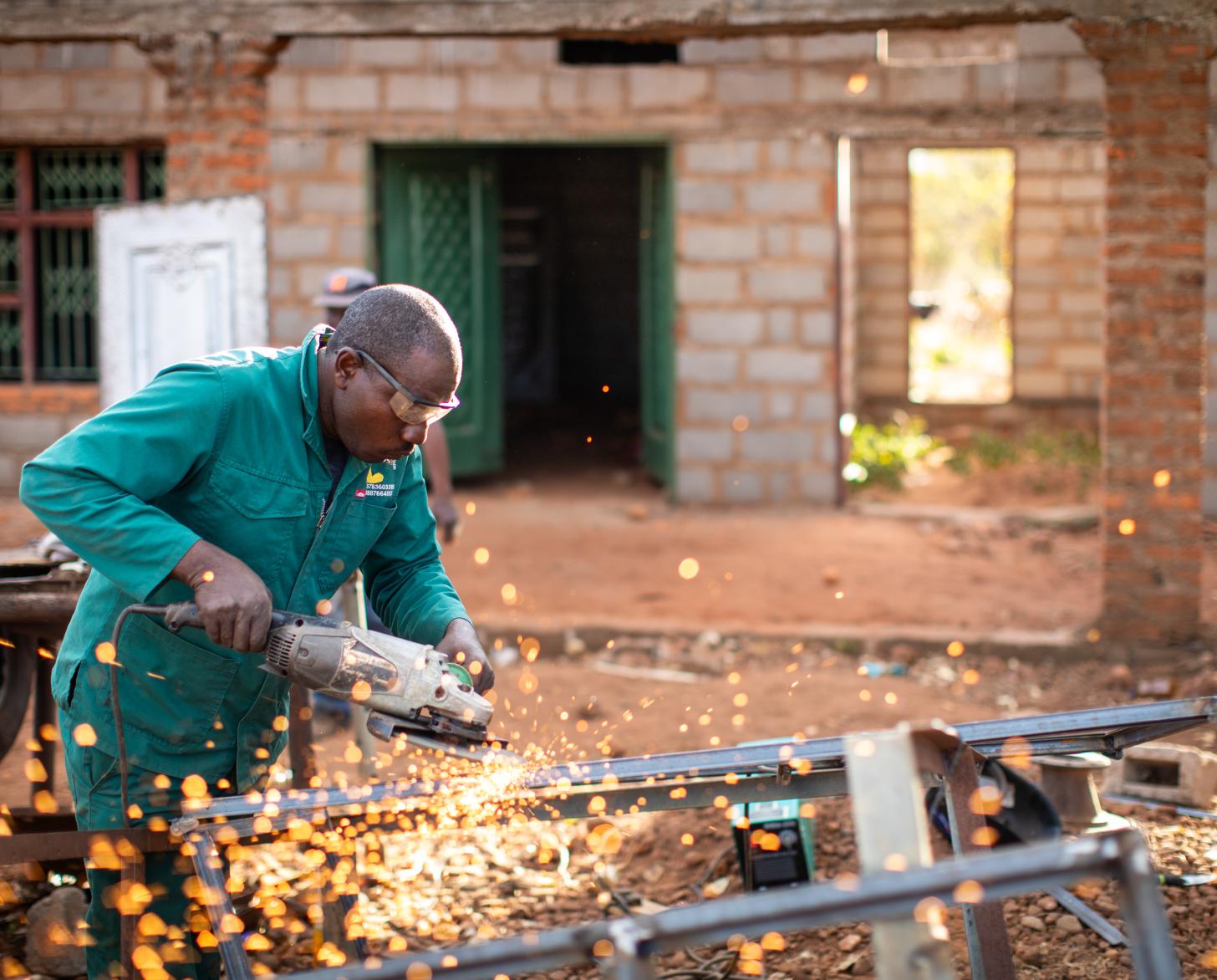 A man in a green suit and goggles fires up an electrical tool as sparks fly.