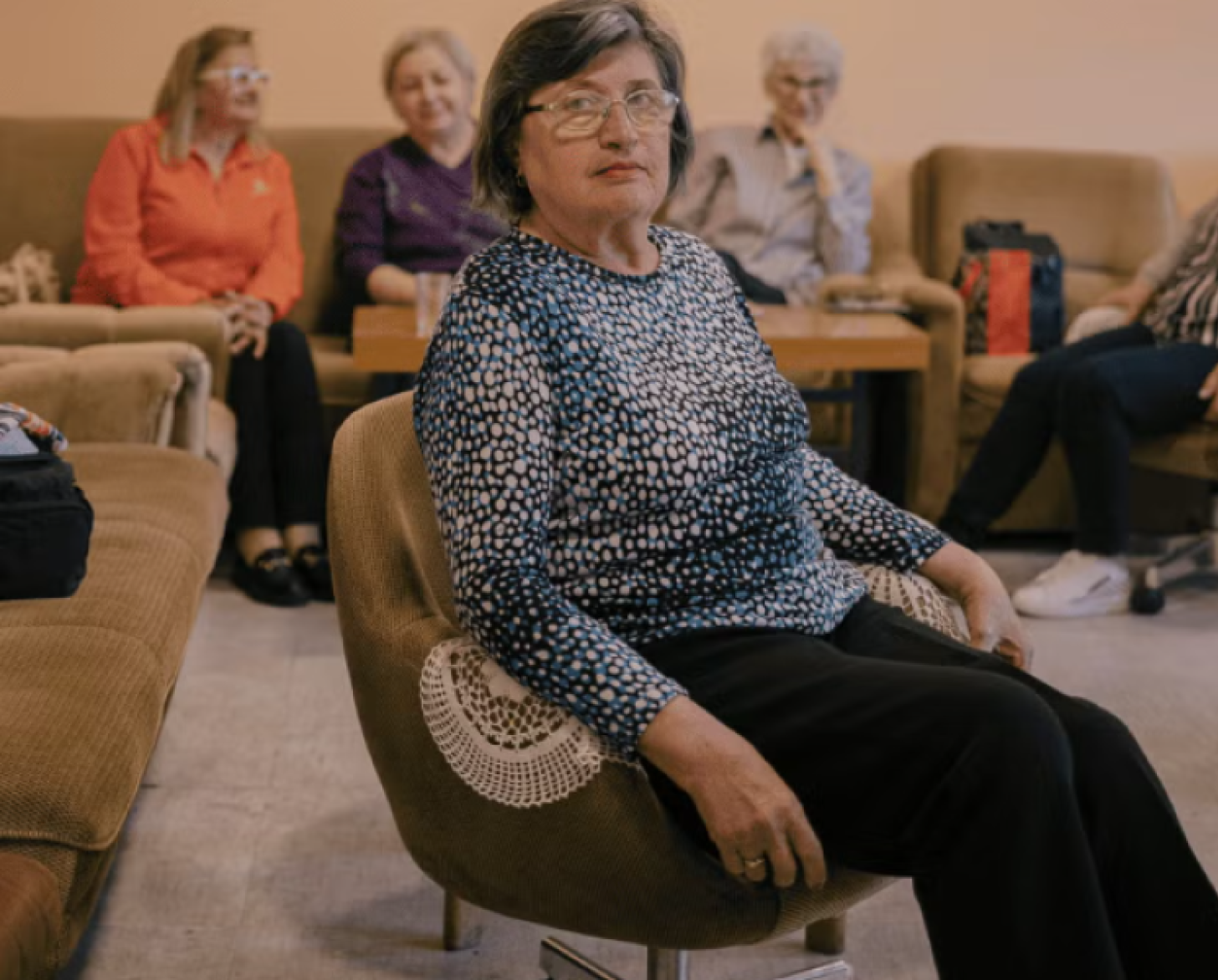 A pensioner in a patterned shirt sits in a brown chair.