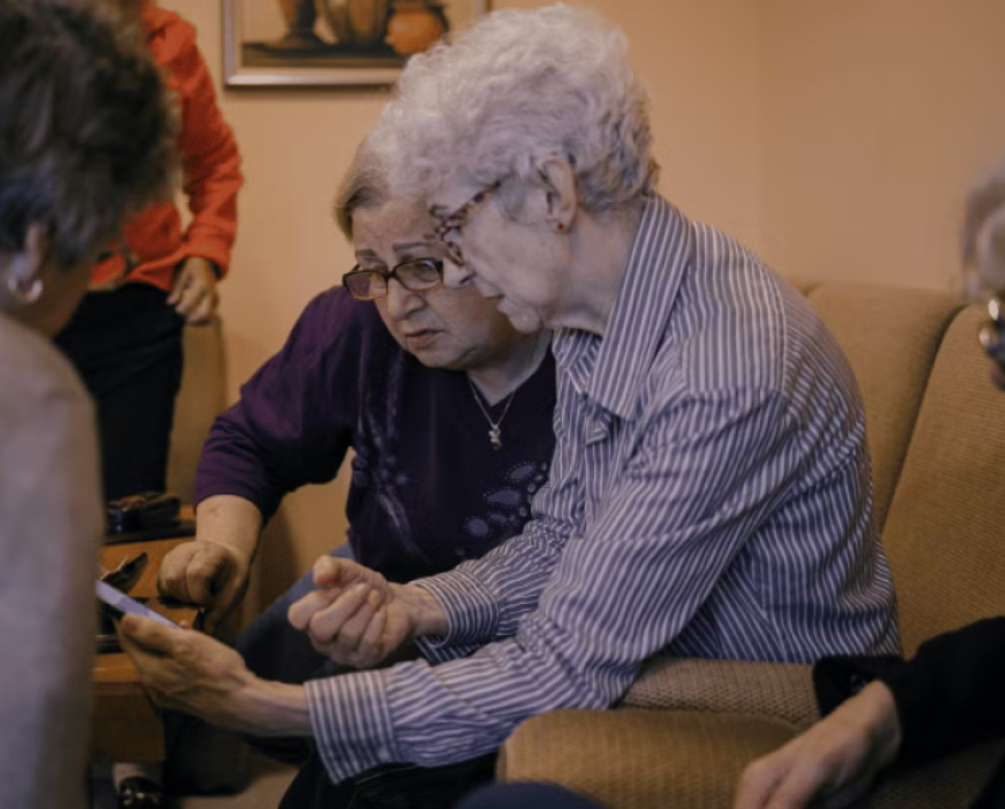 A group of pensioners are gathered around a mobile phone.