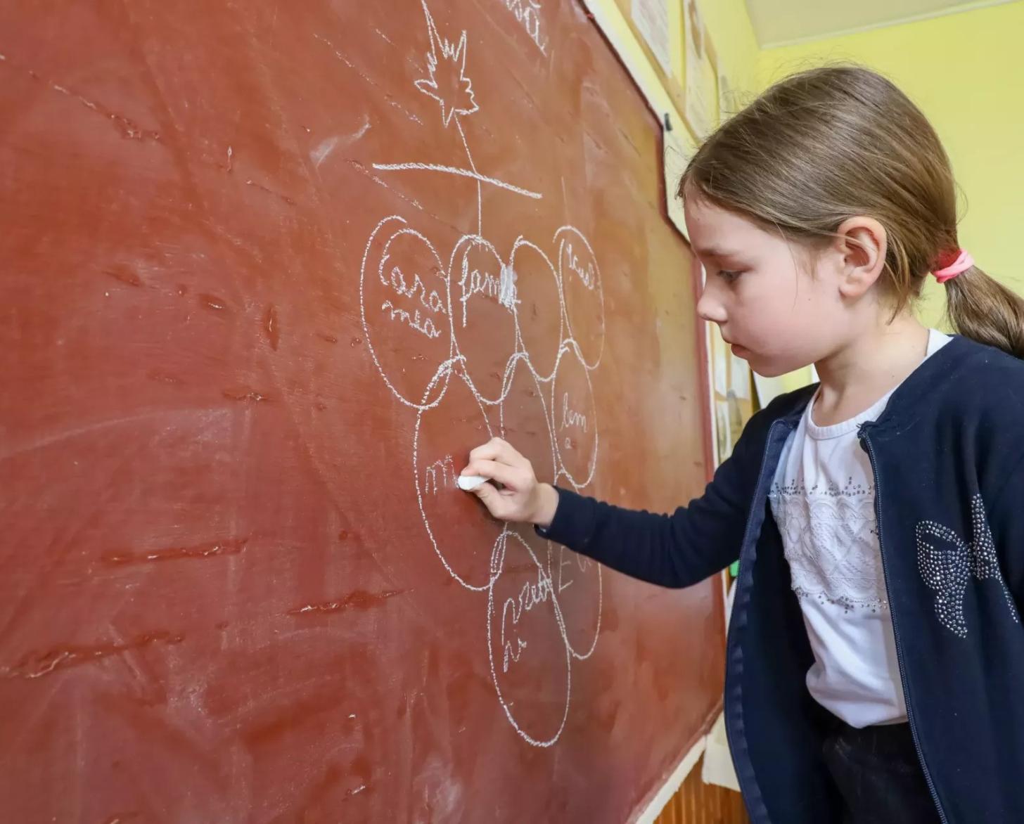 A young Moldovan girl draws on a chalkboard.