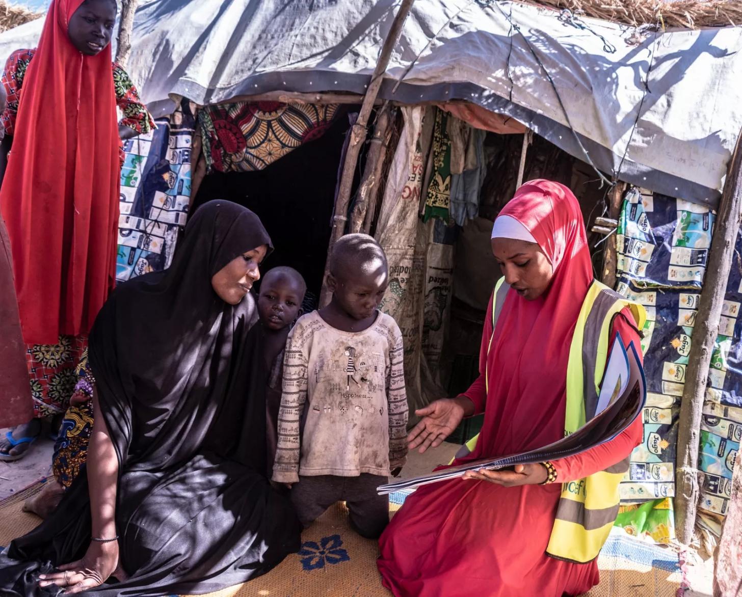 A female volunteer in Nigeria shows a poster to a woman and her four children.