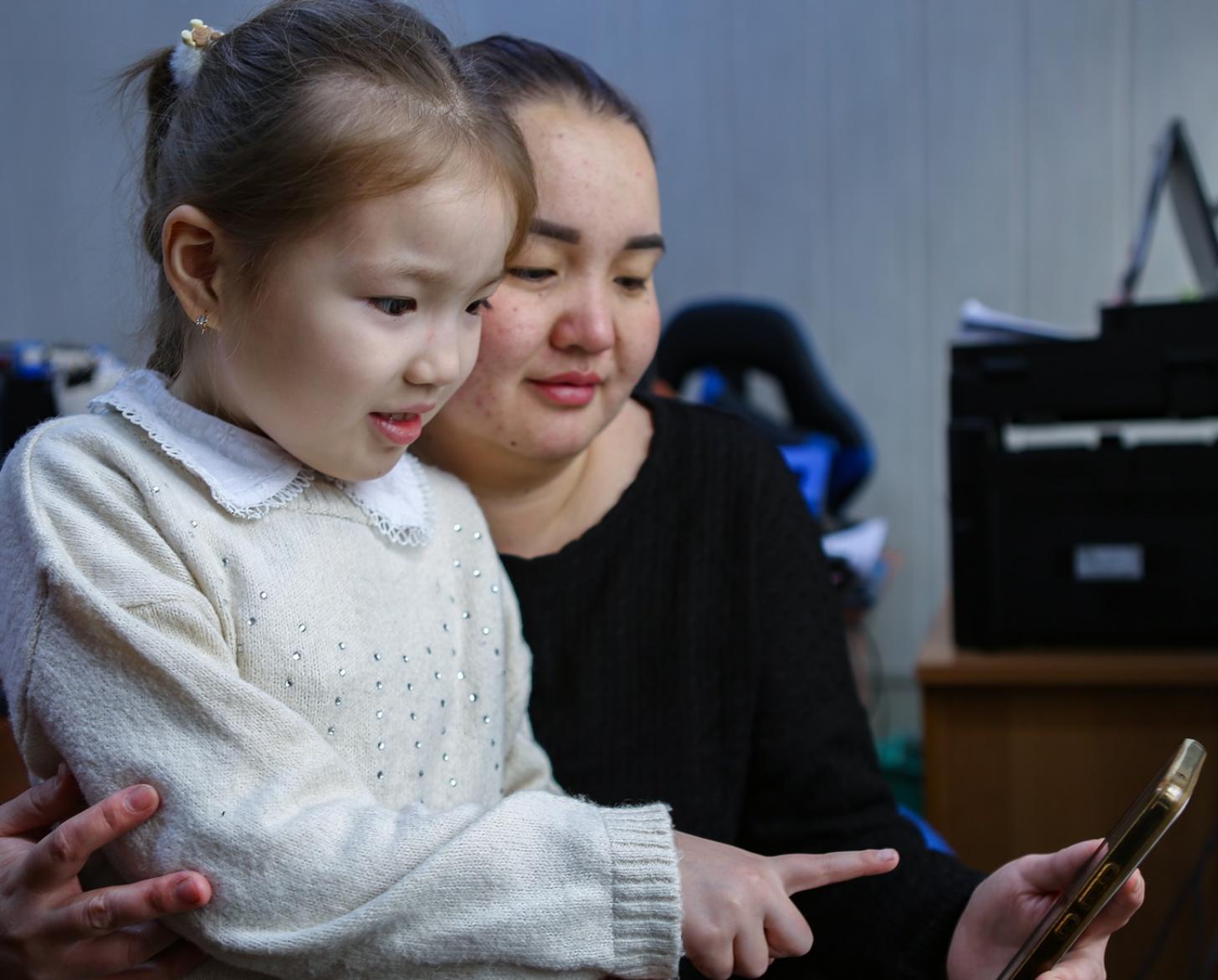 A woman and her daughter in Kyrgyzstan look at a cell phone together.