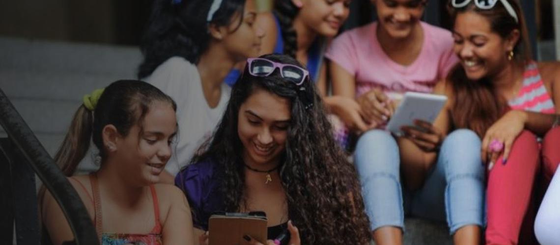 Young women sit together on steps as they cheerfully look at the tablet devices.