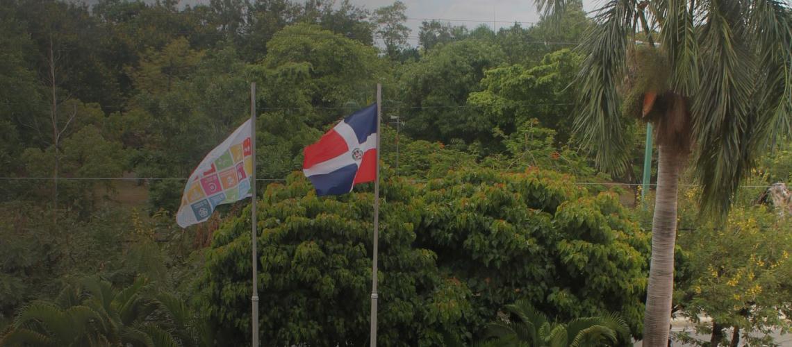 A SDGs flag and the Dominican Republic flag fly high above a lush green countryside.