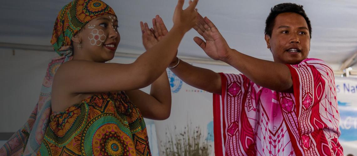 A woman and man dressed in cultural attire touch hands and smile.