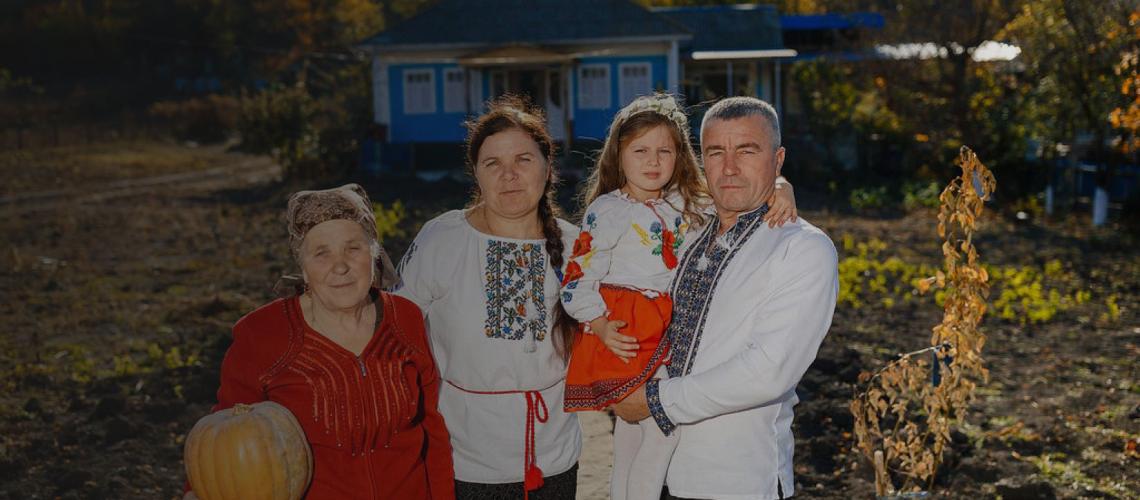 Семья позирует на фоне их небольшого уютного дома.