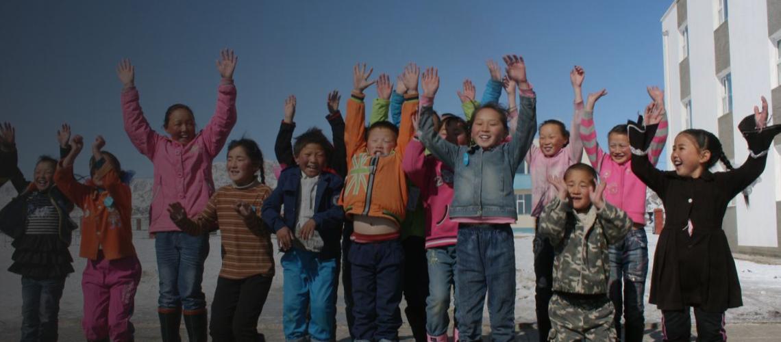 Children excitedly jump in the air and laugh as they attempt to smile at the camera.