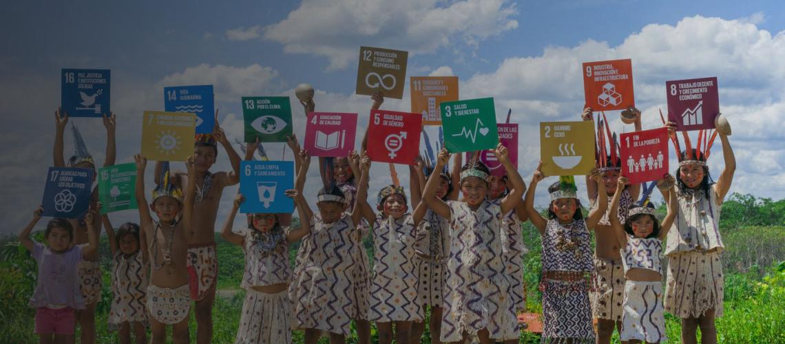 Children wearing traditional clothes from the Communal Amarkaeri Reserve holding SDG signs above their heads. 