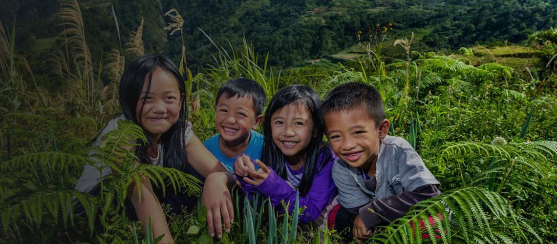 Niños y niñas sentados alegremente en medio de un terreno verde, con hierba y plantas, en la provincia de Benguet, Filipinas.